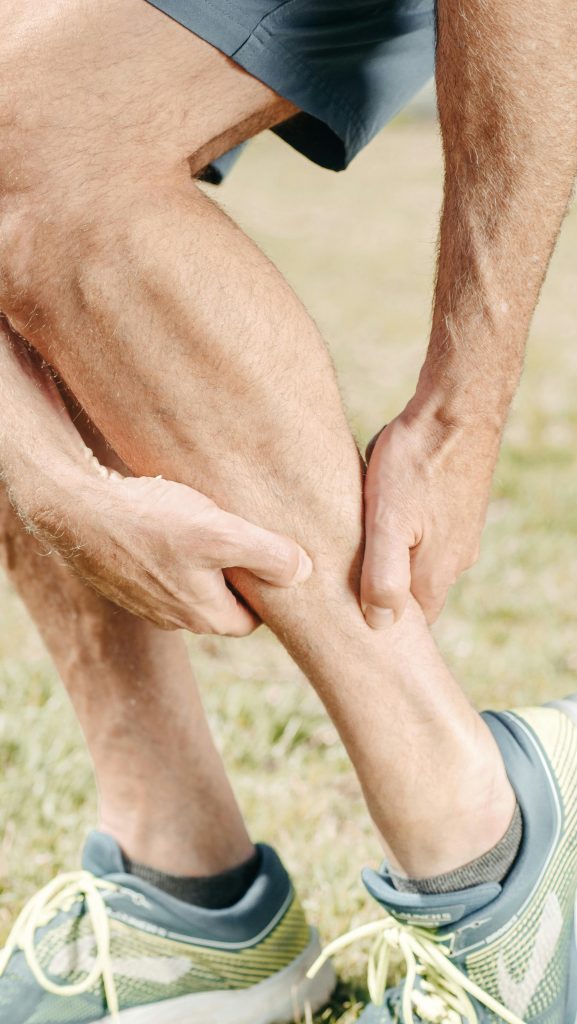 pexels-photo-7298421-7298421 A man outdoors massaging his calf, dealing with muscle pain during sports activities.